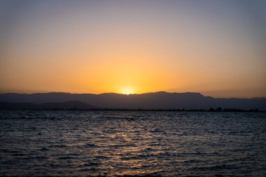 Mavi suları olan kumlu bir sahilde güzel bir gün batımı. Akdeniz 'in rahatlatıcı yaz manzarası. Temiz ve berrak okyanus. Gezegen kavramını sakla. Tatil ekran koruyucusu.
