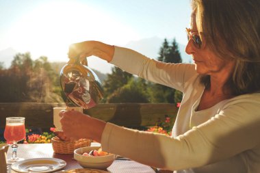 Güneşli bir günde doğada harika bir kahvaltı masasında güzel bir manzarayla eğlenen güzel bir kadın. Sıcak kahveyle sağlıklı bir kahvaltı. Ev yapımı. - Evde. Rahatlama anı.