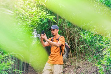Genç, mutlu bir gezgin, güzel bir ormanda sırt çantasıyla yürüyüp fotoğraf çekiyor. Seyahat ve macera konsepti. Kırsalda yürüyüş yapan gençler. Vahşi ve özgürlük hissi. 
