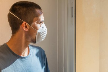 Coronavirus. Corona virüsünün hasta adamı pencereden dışarı bakıyor ve maske takıyor ve evdeki hastalıktan korunuyor. Karantinaya alın. Hasta enfeksiyonu önlemek için izole edilmiş. - Ev. Özgürlük