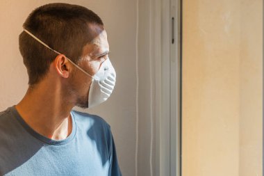 Coronavirus. Corona virüsünün hasta adamı pencereden dışarı bakıyor ve maske takıyor ve evdeki hastalıktan korunuyor. Karantinaya alın. Hasta enfeksiyonu önlemek için izole edilmiş. - Ev. Özgürlük