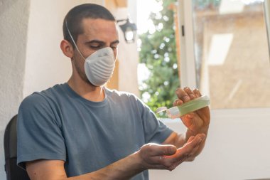 Coronavirus. Karantinadaki adam koronavirüs için koruyucu maske takıyor. Evden çalışıyorum. Ellerini dezenfektan jeliyle temizliyor. Koronavirüsten koru ve genellikle ellerini temizle..