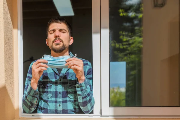 Coronavirus is over, freedom concept man holding his mask and open the window in the sunshine freedom. Coronavirus ended. We won. No more quarantine. Breathe deep. Take off the mask. Cure.