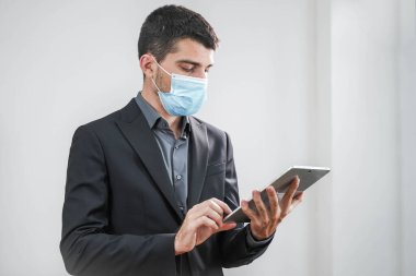 Coronavirus. Beyaz arka planda koruyucu maske takan bir iş adamı. Yüzü maskeli bir iş adamı tecritten sonra işe geri dönüyor. Küçük şirket konsepti. Tabletle çalışmak.