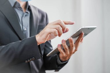 Coronavirus. Beyaz arka planda koruyucu maske takan bir iş adamı. Yüzü maskeli bir iş adamı tecritten sonra işe geri dönüyor. Küçük şirket konsepti. Tabletle çalışmak.