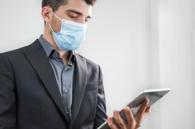 Coronavirus. Beyaz arka planda koruyucu maske takan bir iş adamı. Yüzü maskeli bir iş adamı tecritten sonra işe geri dönüyor. Küçük şirket konsepti. Tabletle çalışmak.