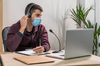 Bilgisayarda çalışan pazarlamacı. Ofiste yüz maskesi takmış bir kulaklıkla konuşuyor. Koronavirüs yüzünden evden izole edilmiş ve çalışıyor. İş çalışanı müşteri çağrılarına cevap veriyor. 