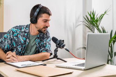 Radyoda radyo sunucusu olarak çalışan adam mikrofonun önünde oturuyor. Genç radyo sunucusu yüz maskeli bir radyo için canlı yayın yapıyor. Evde çalışıyorum. Coronavirüs.
