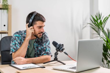 Radyoda radyo sunucusu olarak çalışan adam mikrofonun önünde oturuyor. Genç radyo sunucusu yüz maskeli bir radyo için canlı yayın yapıyor. Evde çalışıyorum. Coronavirüs.