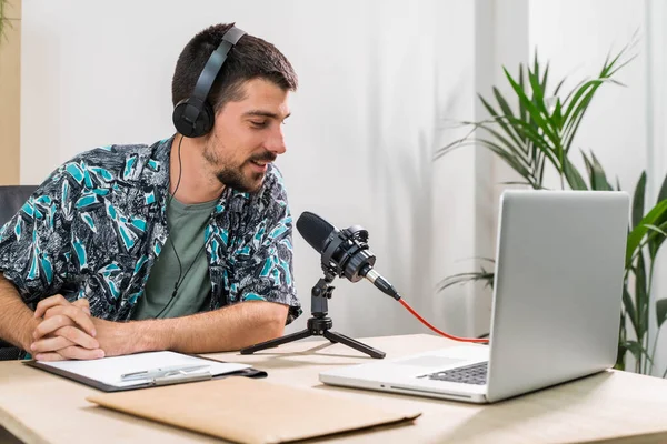 Man working as radio host at radio station sitting in front of microphone. Young radio host moderating a live show for radio with face mask. Working at home. Coronavirus.