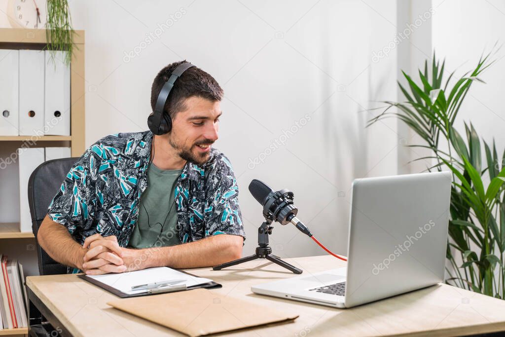 Man working as radio host at radio station sitting in front of microphone. Young radio host moderating a live show for radio with face mask. Working at home. Coronavirus.