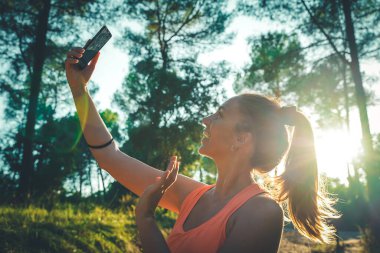 Ormanda akıllı telefonunu kullanarak yürüyen güzel bir genç kız. Genç, mutlu, çekici koşucu kadın, kır yollarında koşuyor... doğa geçmişi sağlıklı yaşam tarzı konseptinde neşeli koşuyor..