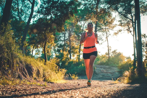 Ormanda yürüyen güzel bir genç kız. Genç, mutlu, çekici bir koşucu kadın. Koşu antrenmanında. Kırsal yolda, doğa arka planında..