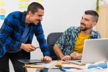 İki iş adamı duvar işaretiyle tartışıp plan yapıyor ve arka planda yapıştırma yapıştırıyor. Başlangıç ofisi. Dizüstü bilgisayarla çalışıyorum. Yaratıcı stüdyo.