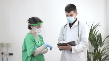 Doktor ve hemşire hastanede konuşuyor. Yüz maskeli bir adam, yüz kalkanı olan bir kadın. Coronavirus koruması. Konuşma ve sınav çalışanları seyahati. Temizlik servisi. Dezenfekte odası. Eldivenler.