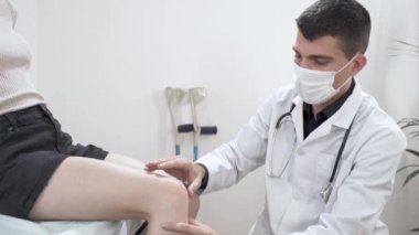 Travma uzmanı doktor hastanın bacağını muayene ediyor. - Ne? Fizyoterapist, fizyoterapi odasında kadın hastanın bacağına masaj yapıyor. Bileğindeki bandaj. Diz incelemesi