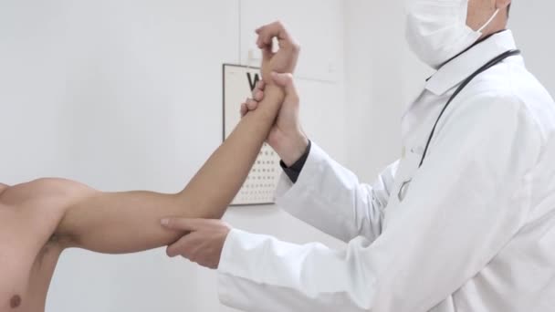 男性の外傷科医を訪問した若い負傷者 医師は患者の手に弾性包帯を適用します 肘の痛み 中年男性の痛み肩 手首を調べる整形外科医の医師 — ストック動画