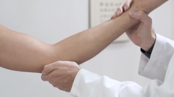 男性の外傷科医を訪問した若い負傷者 医師は患者の手に弾性包帯を適用します 肘の痛み 中年男性の痛み肩 手首を調べる整形外科医の医師 — ストック動画