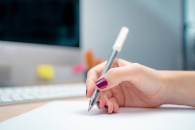 Ofiste çalışan bir iş kadını kağıda yazı yazıyor. Yaratıcı bir stüdyoda sabah. Grafik tasarım, ekran modelleri. gözlük, kalem, klavye, defter, renkler, modern.