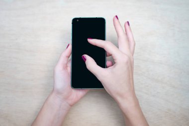 Cep telefonu maketi, ahşap arka planlı siyah ekran. Masada cep telefonuyla mesajlaşan kadın elleri. Reklam metni için arkaplan boşluğu. İnsanlar pazarlama sektörü ve teknolojiyle iletişime geçiyor.