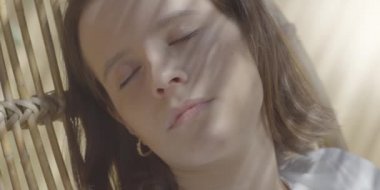 Terasta iskemlede oturan ve güneşi hisseden genç ve tatlı bir kadın. Açık havada uyurken kızın yüzünü kaplayan güzel gölgeler. Sabah ışığı. 