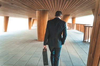 Kendinden emin ve başarılı. Yakışıklı genç işadamı arka planda ofis binası olan evrak çantasıyla dışarı çıkıyor.