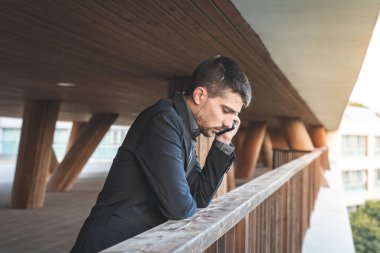 Kendinden emin ve başarılı. Arka planda ofis binası olan yakışıklı bir iş adamı telefonda konuşuyor..