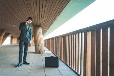 Kendinden emin ve başarılı. Arka planda ofis binası olan yakışıklı bir iş adamı telefonda konuşuyor..