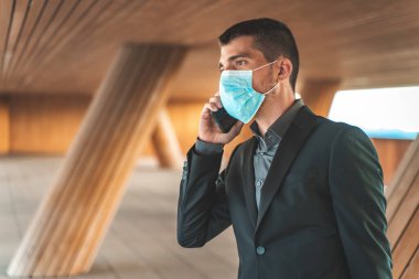 Kendinden emin ve başarılı. Ameliyat maskesi takan yakışıklı genç işadamı arka planda ofis binası olan evrak çantasıyla dışarıda yürürken telefonla konuşuyor. Metin için alanı kopyala.
