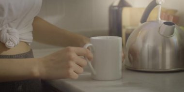 Mutfakta çay hazırlayan genç bir kadın. Evde dinlenme anı. Çaydanlıktan gelen sıcak suyu çay yaprakları içeren bir bardağa dök. Çay demleme süreci.