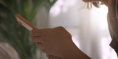 Yatak odasında cep telefonu olan bir kız. Genç bir kadın akıllı telefonuyla yatakta yatıyor. Evde daktilo yazıyorum. 4K Yavaş çekim.