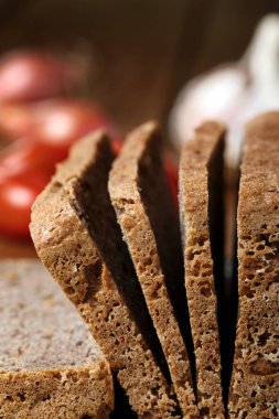 Kesme tahtasında glütensiz karabuğday ekmeği. Arka planda domates, soğan ve sarımsak var.. 