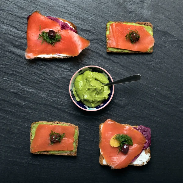 Toasted bread with smoked salmon and guacamole sauce on a black board.