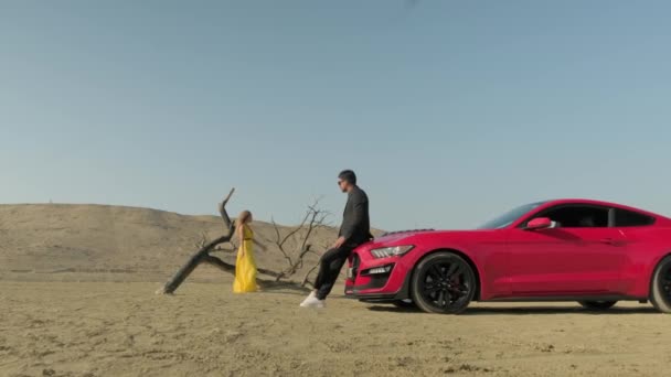 A guy and a girl in yellow clothes in the desert,red car in the desert — Stock Video