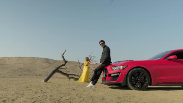 A guy and a girl in yellow clothes in the desert,red car in the desert — Stock Video