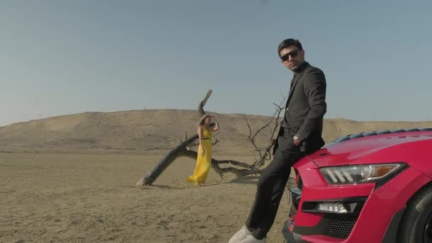 A guy and a girl in yellow clothes in the desert,red car in the desert — Stock Video