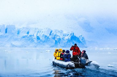 Donmuş turist Almirante Brown, Antarktika Yarımadası yakınındaki arka planda büyük mavi buzul duvarına doğru sürüş ile tekne üzerinde kar yağışı
