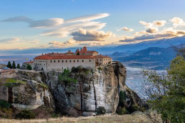 Agios Stephanos or Saint Stephen monastery located on the huge rock with mountains and town landscape in the background, Meteors, Trikala, Thessaly, Greece clipart