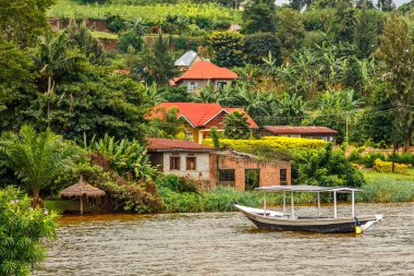 Roof boat anchored at the coast with rwandan village in the back clipart