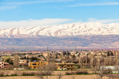 Lebanese houses in Beqaa Valley with snow cap mountains in the b clipart