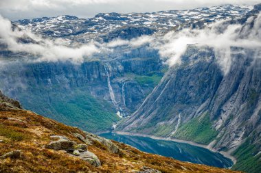 Bulutların içinde saklanan sarp kayalıklarla çevrili mavi göl, Odda, Hor