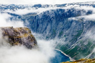 Bulutların içinde saklanan sarp kayalıklarla çevrili mavi göl, Odda, Hor
