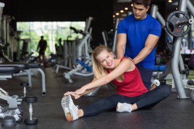 Genç beyaz kadın spor salonunda Asyalı erkek antrenörle tartılmaya odaklanıyor. Spor ve eğlence konsepti.