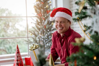 Hediye kutusuyla Noel ağacının yanında oturan genç beyaz bir adam. Gülümseyen Noel 'i kutlayan mutlu anlar.