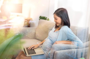 Güzel, mutlu, koca göbekli, bilgisayar kullanan Asyalı hamile kadın. Hamilelik, annelik, insanlar ve beklenti konsepti..
