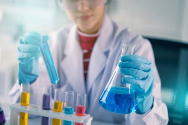 Genç Asyalı tıp teknisyeni kadın deney tüpüyle test yaparken bilim laboratuarında araştırma yapıyor.