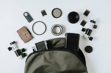 Eski kamera, yeşil sırt çantası ve soluk arkaplanda fotoğraf aksesuarları.