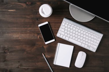 Tahta arka planda beyaz klavye, fare ve not defteri. Düz yatış ve üst görünüm