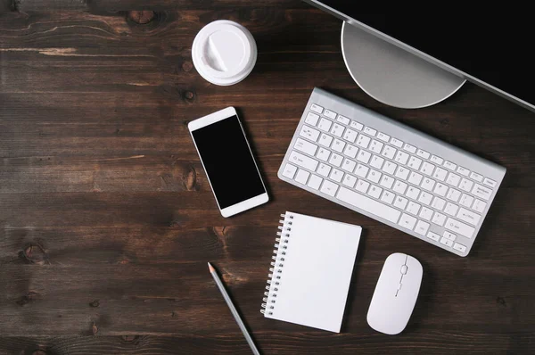 Tahta arka planda beyaz klavye, fare ve not defteri. Düz yatış ve üst görünüm