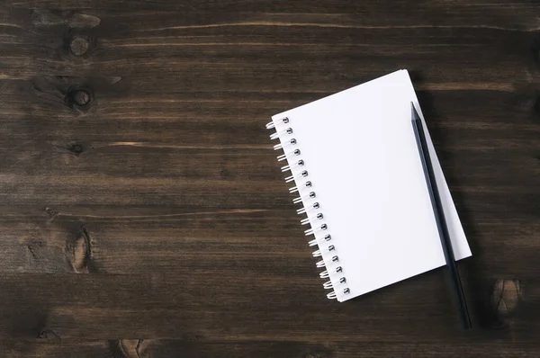 Beyaz Not Defteri ve koyu ahşap arka planda siyah bir kalem.